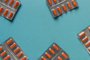 Blisters of tablets with orange capsules on a plain blue background. Pharmacy products. Medicine...