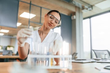 Working with bunch of test tubes. Female doctor in white coat is indoors