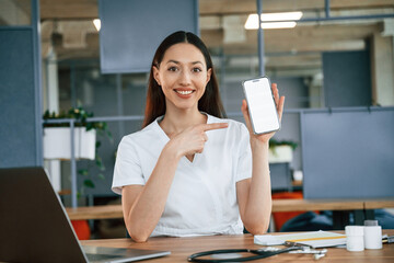 Holding smartphone with copy space on display. Female doctor in white coat is indoors