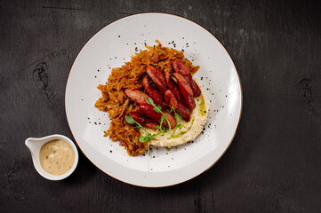 A dish of mashed potatoes with stewed cabbage and fried sausages on a dark wooden background