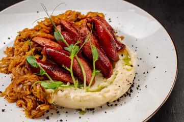 A dish of mashed potatoes with stewed cabbage and fried sausages on a dark wooden background