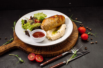 A dish of mashed potatoes with a steam cutlet and salad and ketchup on a wooden background