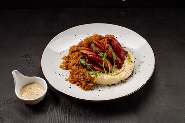 A dish of mashed potatoes with stewed cabbage and fried sausages on a dark wooden background
