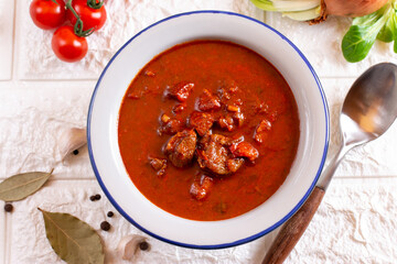 Pork goulash meat on plate, garlic, onion, tablecloth in the background - typical Czech food