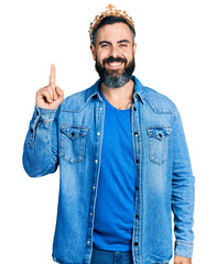 Hispanic man with beard wearing king crown pointing finger up with successful idea. exited and happy. number one.