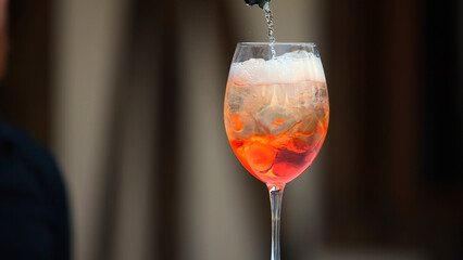 Drink slowly pours into glass. Ice cubes and colorful beverage. Dry wine for Aperol Spritz. First layer of cocktail.