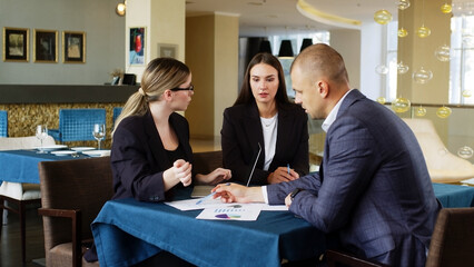 Close-up group of people talking in budget plan report with brief presentation of chart data in paper work on laptop at table in office of tax credit consultant, stock broker or trader.