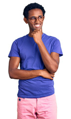 Fototapeta premium African handsome man wearing casual clothes and glasses with hand on chin thinking about question, pensive expression. smiling with thoughtful face. doubt concept.