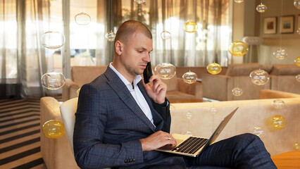 Successful business man in a stylish suit uses typing on a laptop while concentrating on online communication in the hotel lobby. People and modern technology concept.