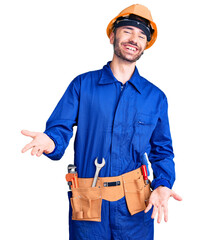 Young hispanic man wearing worker uniform smiling cheerful with open arms as friendly welcome, positive and confident greetings