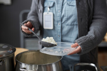 Close up of unrecognizable young woman volunteering at soup kitchen and putting hot rice on plastic plates, copy space