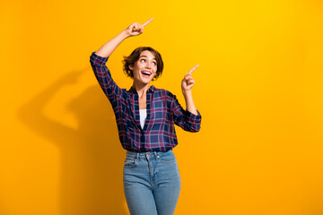 Photo of overjoyed woman dressed plaid shirt look directing at impressive discount empty space isolated on yellow color background