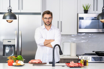 Handsome man is preparing food in kitchen. Handsome mature middle-aged man cooking meat in kitchen. Man preparing food meal in kitchen. Healthy food and cooking in kitchen concept.