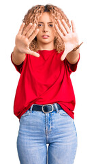 Young blonde woman with curly hair wearing casual red tshirt doing frame using hands palms and fingers, camera perspective