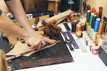 Close up of a shoemaker or artisan worker hands. Leather craft tools on old wood table.