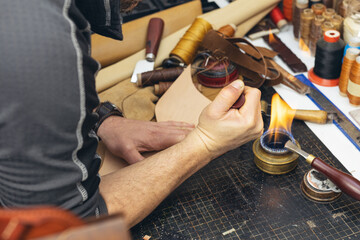 Close up of a shoemaker or artisan worker hands. Leather craft tools on old wood table.