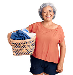Senior woman with gray hair holding laundry basket looking positive and happy standing and smiling...