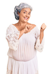 Senior woman with gray hair wearing bohemian style pointing to the back behind with hand and thumbs up, smiling confident