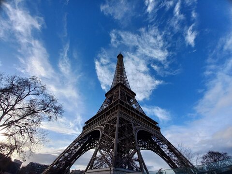 Foto dal basso verso l'alto della Torre Eiffel a Parigi in Francia, con cielo azzurro e poche nuvole e rami spogli degli alberi