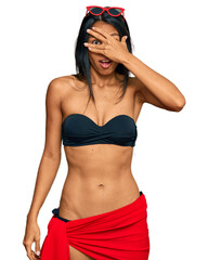 Young african american woman wearing bikini peeking in shock covering face and eyes with hand, looking through fingers with embarrassed expression.