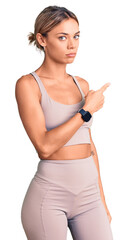Fototapeta premium Beautiful caucasian woman wearing sportswear pointing with hand finger to the side showing advertisement, serious and calm face