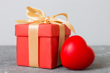gift box with red bow and red heart on colored background. Perspective view. Flat lay