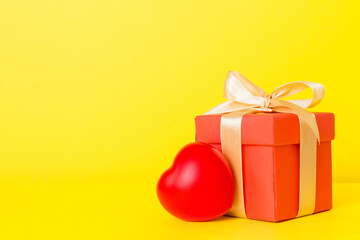 gift box with red bow and red heart on colored background. Perspective view. Flat lay