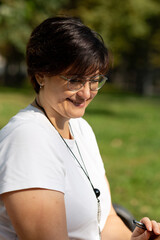A beautiful middle-aged woman with glasses and short dark hair is sitting on a bench