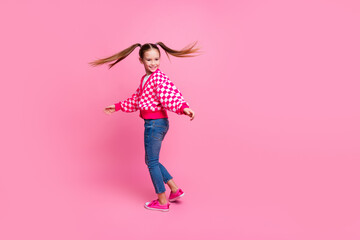 Full size photo of positive schoolgirl with tails dressed knit cardigan turning around near empty space isolated on pink color background