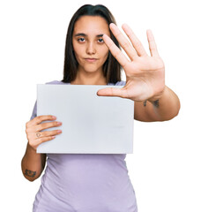 Fototapeta premium Young hispanic woman holding blank empty banner with open hand doing stop sign with serious and confident expression, defense gesture