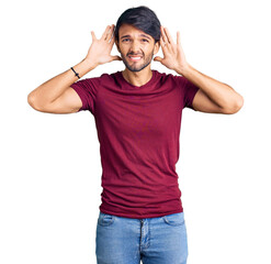 Handsome hispanic man wearing casual clothes trying to hear both hands on ear gesture, curious for gossip. hearing problem, deaf