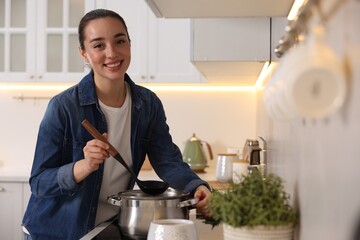 Smiling woman with ladle cooking soup in kitchen - obrazy, fototapety, plakaty