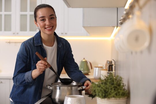 Smiling woman with ladle cooking soup in kitchen