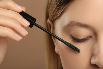 Fototapeta premium Woman applying mascara onto eyelashes against light brown background, closeup