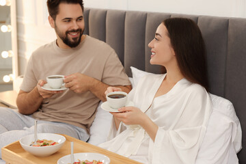 Happy couple having breakfast on bed at home
