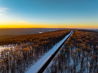 aerial view of the treetops of the forest and a road illuminated by the setting sun during winter in moldova