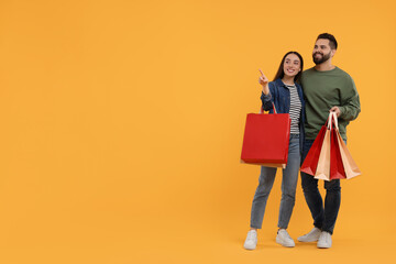 Happy couple with shopping bags looking at something on orange background. Space for text