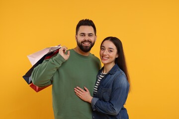 Fototapeta premium Happy couple with shopping bags on orange background