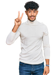 Young arab man wearing casual winter sweater smiling with happy face winking at the camera doing...