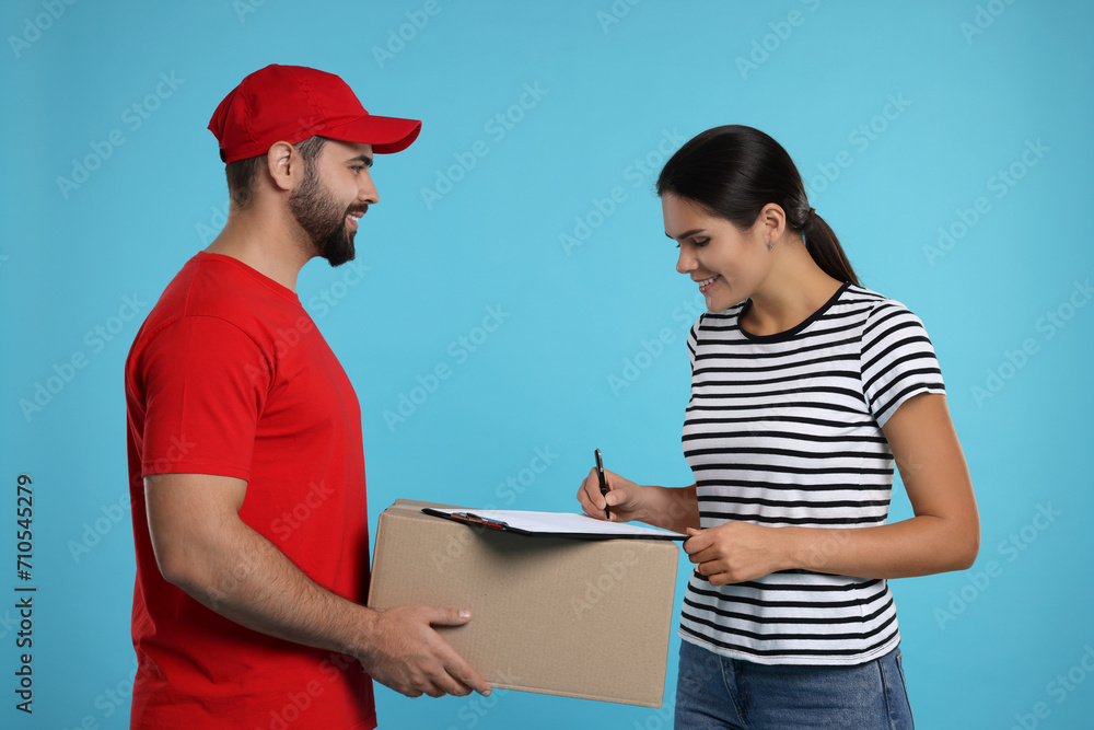 Poster Smiling woman signing order receipt on light blue background. Courier delivery