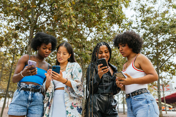 Smiling friends using phone standing in a park