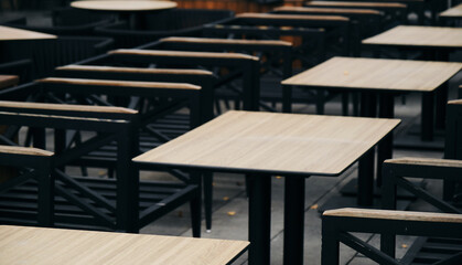Empty wooden tables and chairs in the cafe on the veranda in low season. The restaurant is ready to receive guests. A minimalistic blurred background for advertising a coffee chain.