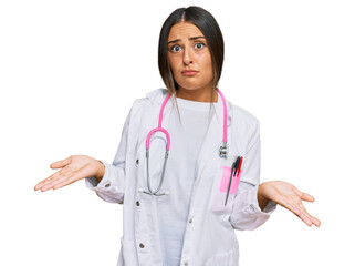 Beautiful hispanic woman wearing doctor uniform and stethoscope clueless and confused expression...
