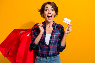 Portrait of overjoyed ecstatic girl wear checkered blouse hold new clothes demonstrate credit card...