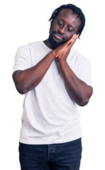 Young african american man with braids wearing casual white tshirt sleeping tired dreaming and posing with hands together while smiling with closed eyes.