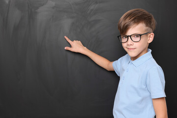 Cute schoolboy in glasses near chalkboard, space for text