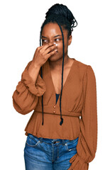 Young african american woman wearing casual clothes smelling something stinky and disgusting, intolerable smell, holding breath with fingers on nose. bad smell