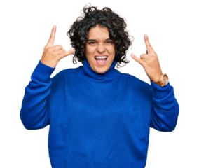 Young hispanic woman with curly hair wearing turtleneck sweater shouting with crazy expression doing rock symbol with hands up. music star. heavy music concept.