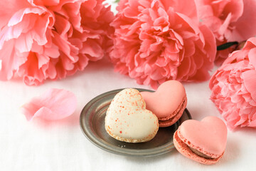 Pink coral peony flowers and french sweet cookies heart shape macarons macaroons on linen table cloth background.