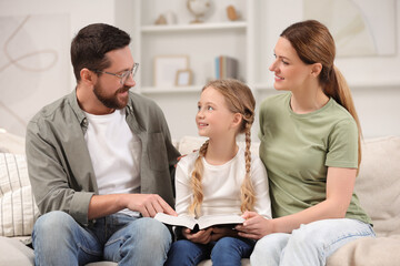 Girl and her godparents reading Bible together on sofa at home